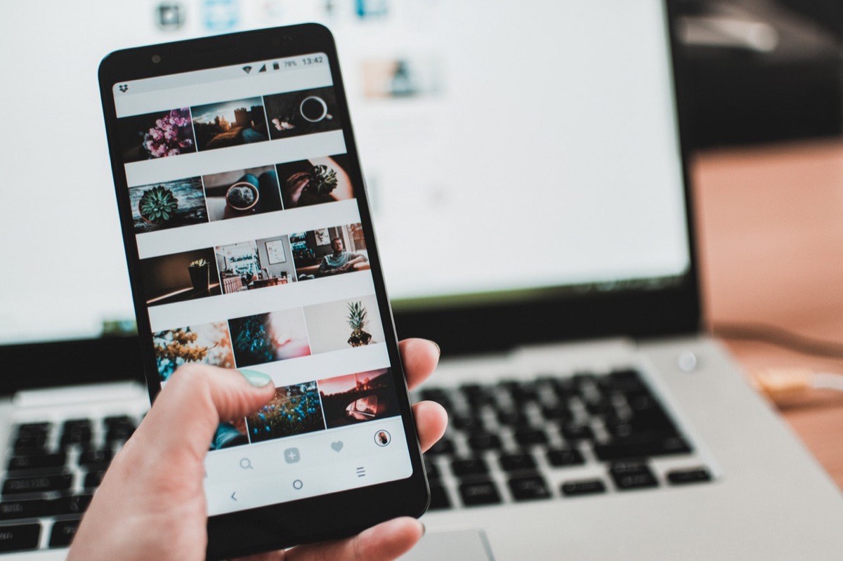 Feed Instagram affiché sur un smartphone tenu devant un ordinateur portable