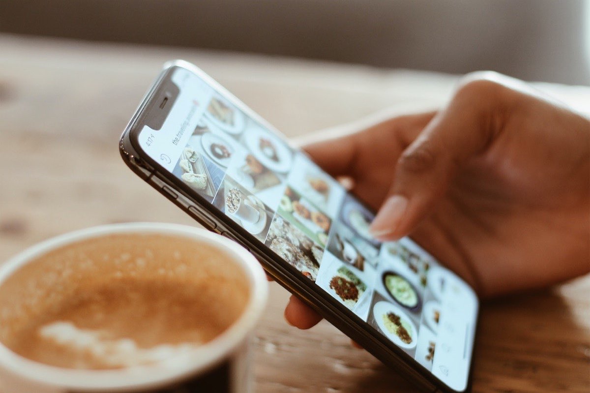 Vendre ses produits en ligne : main tenant un smartphone affichant un feed Instagram, à côté d’un cappuccino